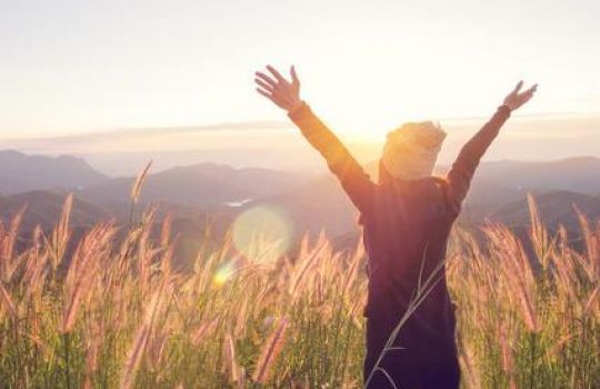 Frau steh vor Gebirge im Sonnenschein und breitet Arme aus