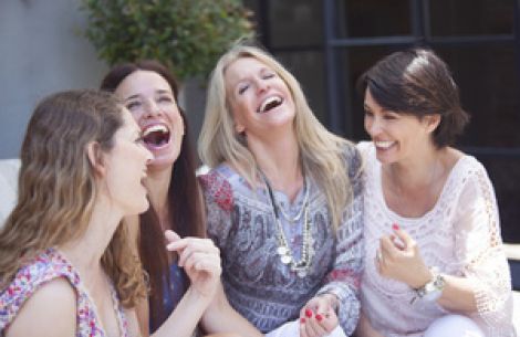 Vier Frauen sitzen fröhlich auf dem Sofa und lachen ausgelassen.