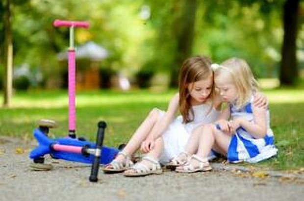 Junges Mädchen tröstet ihre Schwester, diese hat eine kleine Wunde auf dem Knie.