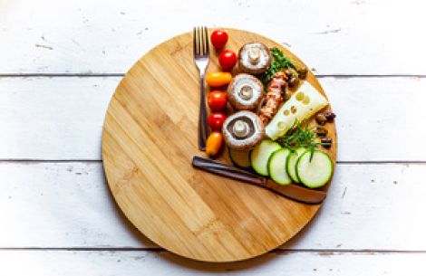 Auf einer runden Holzplatte ist nur in einem Viertel gesundes Essen zu sehen, der andere Teil der Holzplatte ist leer.