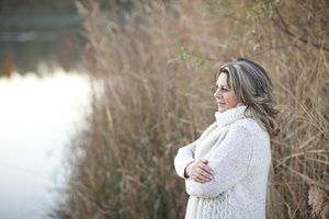 Frau im Wollpullover schaut auf den See und schlägt der Herbstdepression ein Schnippchen.